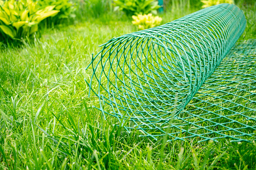 roll of plastic mesh is lying on the lawn. plastic mesh is ready for use in the garden.