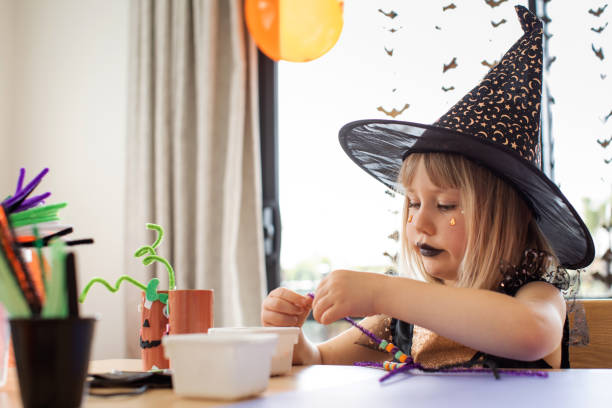 uma garota fofa em uma fantasia de bruxa faz uma aranha engraçada para o halloween com suas próprias mãos. artesanato infantil para o halloween - child autumn craft preschooler - fotografias e filmes do acervo