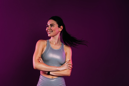 Happy woman athlete with crossed arms against a magenta background