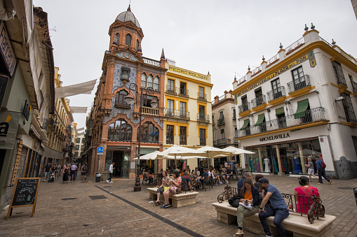 Historic buildings in Plaza Del Pan, Seville, Spain. Tourists seen walking and sitting in the little square.