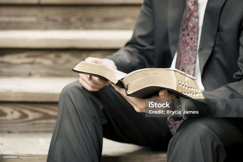 Missionary Sitting on Stairs Reading from the Scriptures A male missionary dressed in a suit sits on wooden stairs and reads from the Scriptures. Missionary Stock Photo