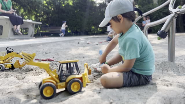 Playful Child Engages with Toy Tractors and Shovel in Sandbox Playground - Daytime Fun