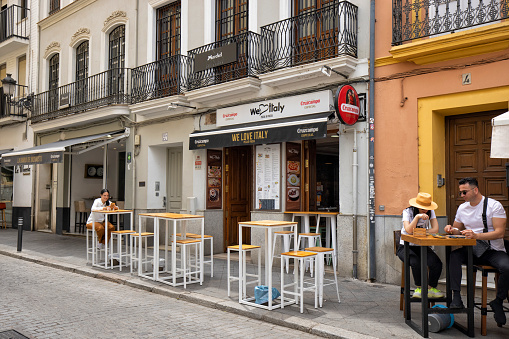 People sitting at tables in the sidewalk outside of an Italian restaurant, Seville, Spain.