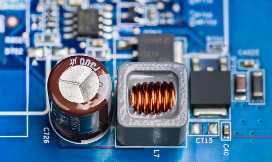 Brown electrolytic capacitor, inductor in gray housing and black transistors or microchip on a blue PCB. Electrotechnology