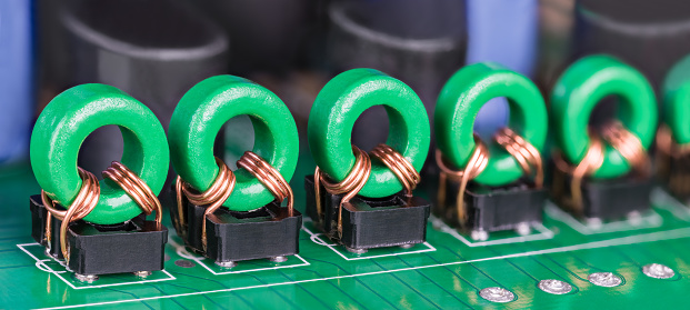 Closeup of electronic coils with copper wire on green ferrite core in black holders on printed circuit board
