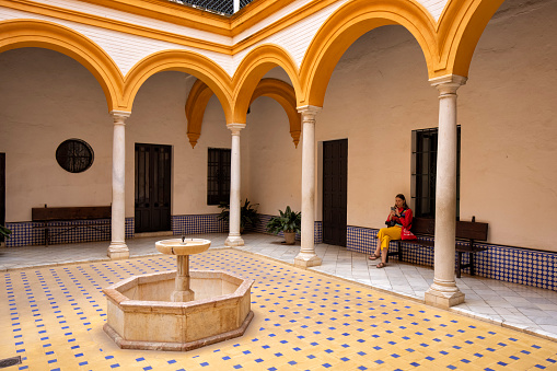 A woman sitting on the bench in the patio with fountain, Alcazar of Seville, Spain.