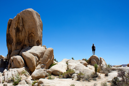 A man standing on the rock looking far into the distance. Solo travel. Exploring. Arch Rock Trail, Joshua Park National Park, California, USA.