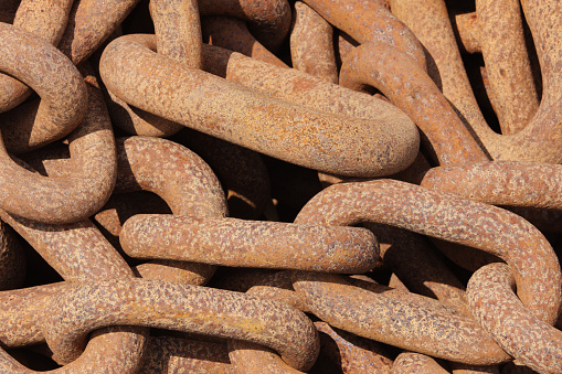 Large rusted anchor chain links piled in a heap fill this horizontal frame entirely - close up, tightly cropped.  The single color in the image is rust-color, aside from shadow areas among the links.