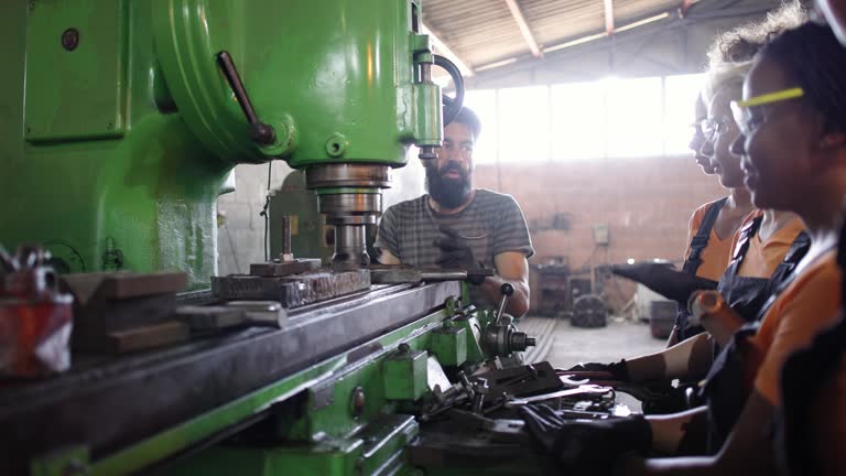 Caucasian male metallurgical engineer, trains group of multiracial female workers how to work on a milling machine