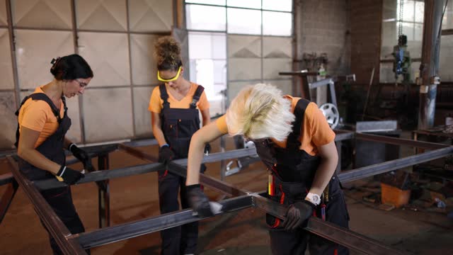 Caucasian female metal workers, sanding an metal construction frame, at the metal factory