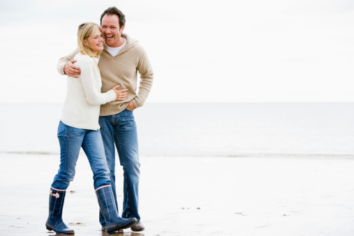 Couple walking on beach arm in arm smiling chatting to each other laughing