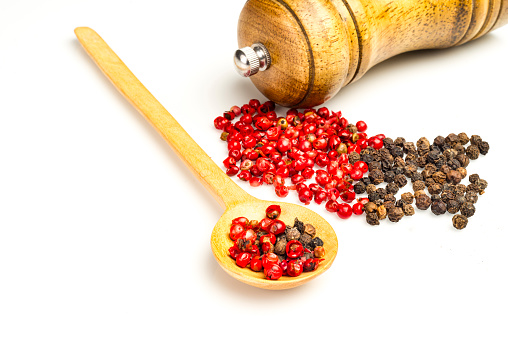 Black and red seasoning pepper with wood spoon and mill over white table in the kitchen at home.Image made in studio