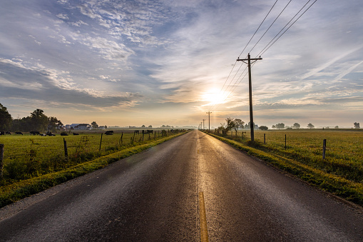 The morning mist hangs in the air as the sun rises over a rual landscape with a rural road.