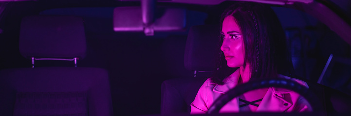 Female portrait of one woman indoors the car. Neon light concept photography, futuristic photo with color lighting indoors the vehicle. Asian girl is driver.