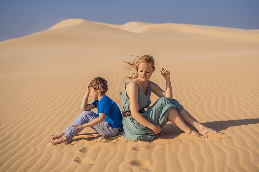 Relationship problems between mother and son. Family conflict. Mom and son have a heated relationship, sit in the hot desert with their backs to each other and do not want to talk.