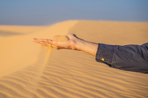 Desert, sand puffs through the fingers of a mans hand.