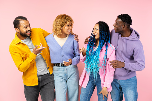 Portrait of attractive smiling African American friends wearing stylish casual outfit communication, talking isolated on pink background. Friendship