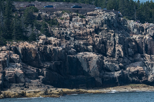 Otter Cliffs viewed from boat on Frenchman Bay with cars on road visible at top of image.