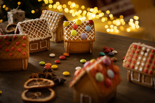 Christmas house made of gingerbread cookies decorated with sugar icing on blue background with bokeh garland.