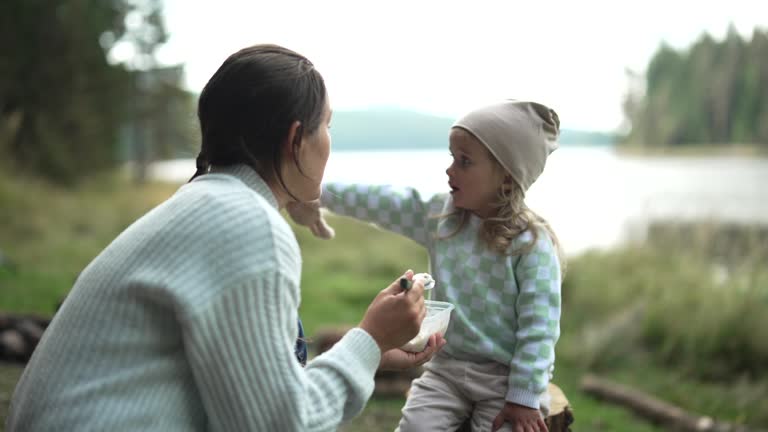 Family camping at lake. Mom feeds kid in nature.