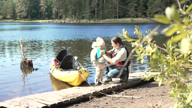 Mom and kid prepare to go kayaking at lake.