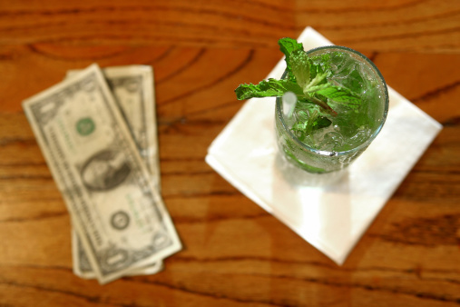 Mojito on a napkin on a bar with dollar bills next to it.