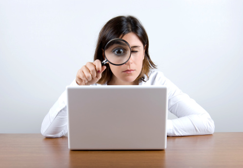 woman looking to laptop with magnifying glass