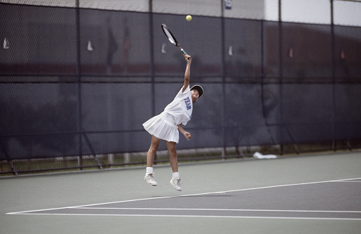 female junior tennis player competing in a tournament.  Serving tennis ball. Image was photographed with high speed film and scanned on a high Resolution scanner.  Image has film grain.