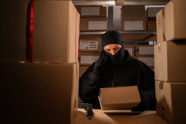 istock Thief stealing a box in a warehouse calls on a mobile phone at night. Concept of problems with the theft of goods and parcels at the post office. 1738087070