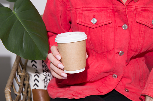 A woman holds a disposable beige kraft coffee cup in her hands.