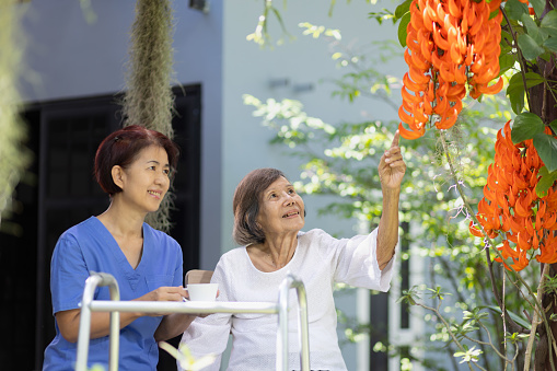 Smiling elderly woman in garden. Happy senior woman relaxing on terrace with caregiver at home.
