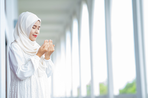 The image of an Asian Muslim woman in the Islamic religion in hijab in white color. reading the Quran, Koran Asian Muslim woman in the Islamic religion in hijab in white color, Arabic word translation: The Holy Al Quran.