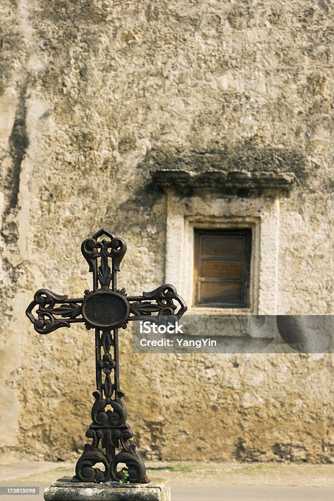 Iron Cross "Subject: Vertical view of a rustic wrought iron cross in the foreground, with a wall detail of a mission in the background.Location: Mission San JosA, San Antonio, Texas" Religious Cross Stock Photo