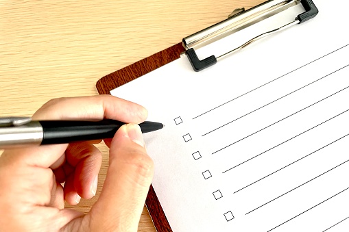 A person's hand taking notes on a checklist