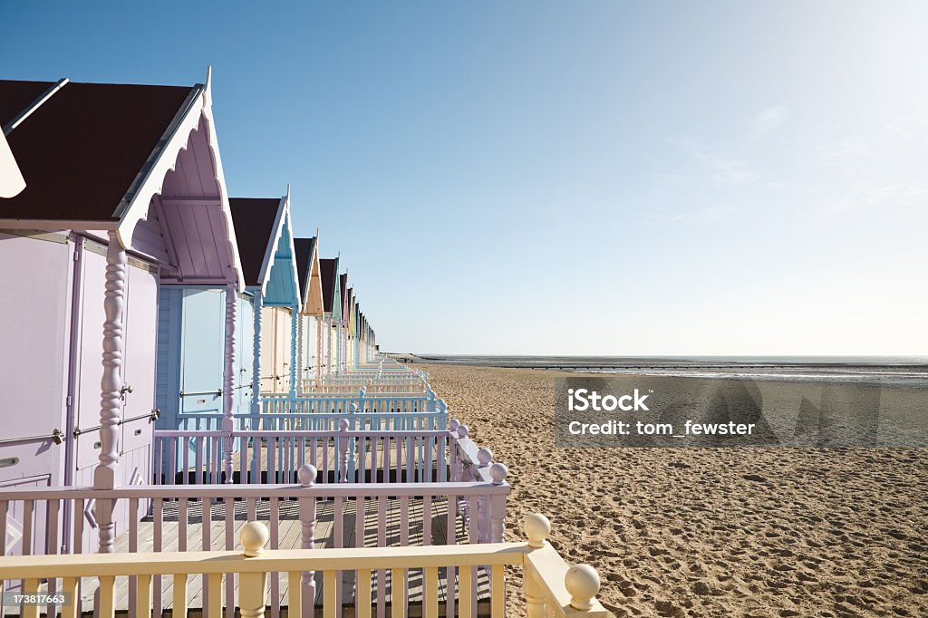 A row of pastel colored beach homes on the sandy shore Row of beach huts in West Mersea, Essex, England Beach Stock Photo