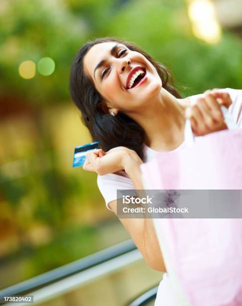 Foto de Animado Jovem Mulher Segurando O Cartão De Crédito E Carregando Sacos De Compras e mais fotos de stock de 20 Anos