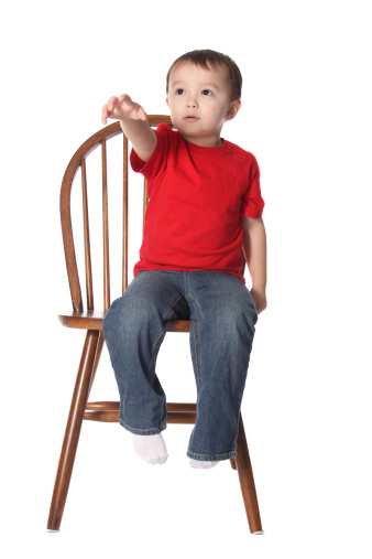 Toddler boy reaching for something while sitting in a chair