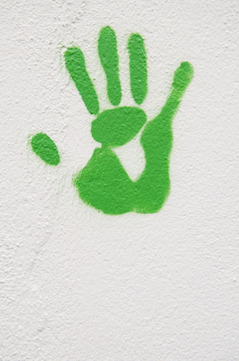 Print of an outstretched hand in green paint on a white wall