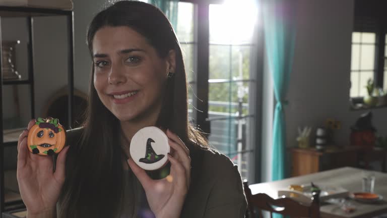 Charming young woman holding Halloween themed cookies and smiling at camera