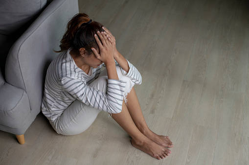 Asian woman sitting on floor at home feeling sad tired and worried suffering depression in mental health.Female suffer from mental health problems.