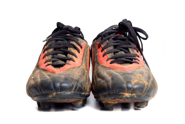 Composite image. Cropped photo of male soccer player in white shorts and red socks tying shoelaces on cleat while standing on green grass field. Concept of sport, football, pre-game preparation