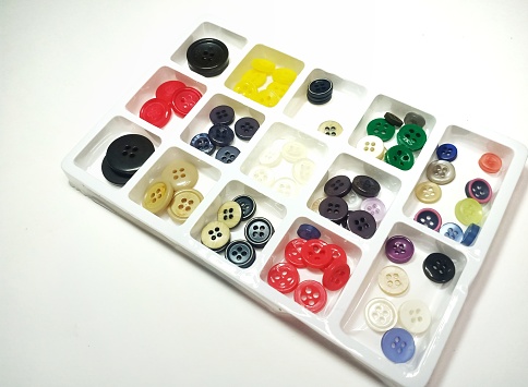 Colored buttons are lined up in a white plastic box. Various colors such as red, yellow, black, etc. are placed on a white background.