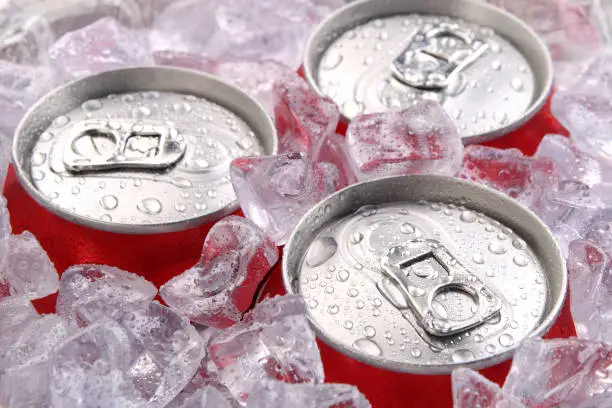 Photo of Close up of the tops of three soft drink cans in ice