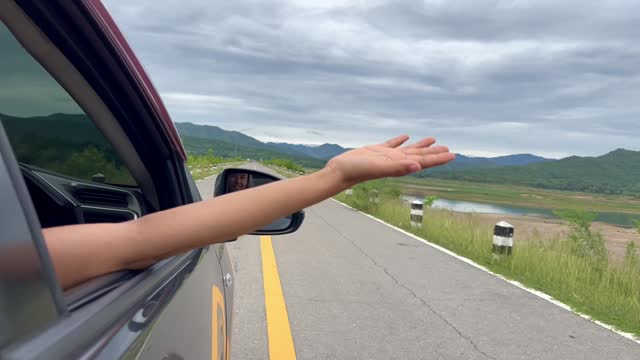 Woman driving a car and stretching out her arms to play in the wind.