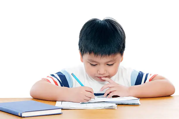 Elementary school boy doing his schoolwork and biting his nail. Isolated on white background.