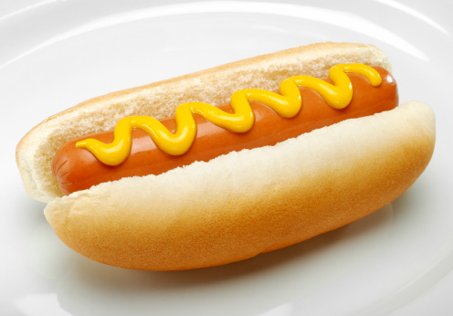 Hot dog with mustard in a white plate. More hot dogs...