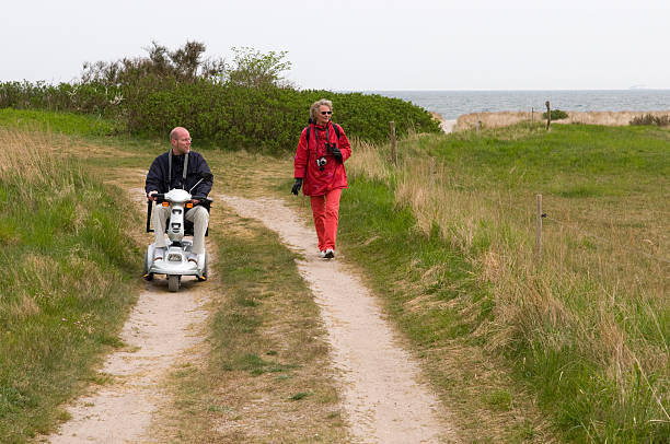 Senior man in scooter and woman walking on nature path stock photo
