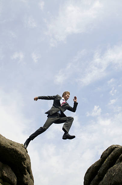 istock Businessman Jumping Outdoors Over Valley Between Rocks 173840873