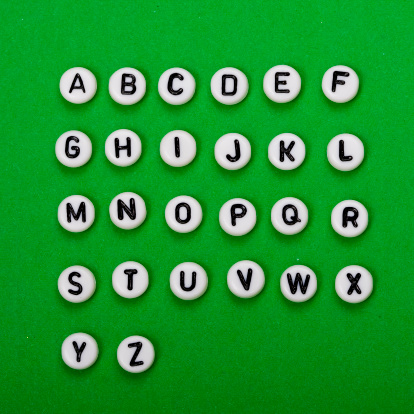 Alphabet written on beads on green background.