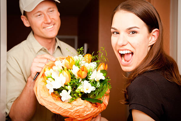 Bouquet of fresh flowers in the foreground while mother and daughter decorate a gift box together in the background. Cozy home lifestyle scene symbolizing family bonding, celebration, and handmade gift preparation.